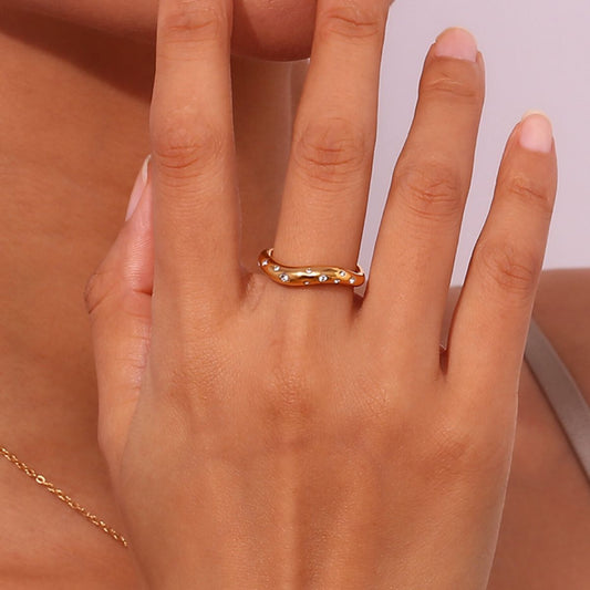 Modelo luciendo el anillo Aere dorado con circonitas, una pieza de acero resistente al agua con diseño orgánico.