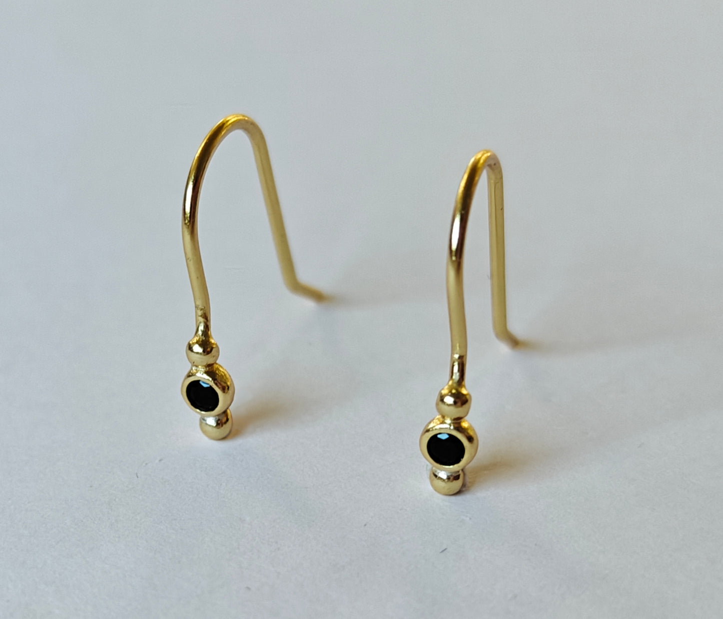 Primer plano frontal de pendientes de plata bañados en oro de 18 quilates con detalle de circonita negra, joyería contemporánea Malbae para uso diario.