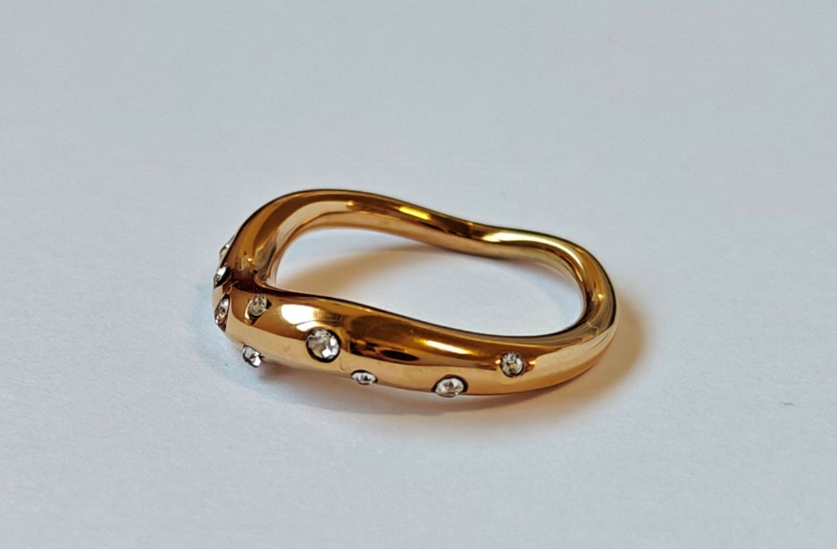 Primer plano detallado de las circonitas blancas engastadas sobre la banda ondulada del anillo Aere de acero inoxidable con baño de oro de 18k de MALBAE.