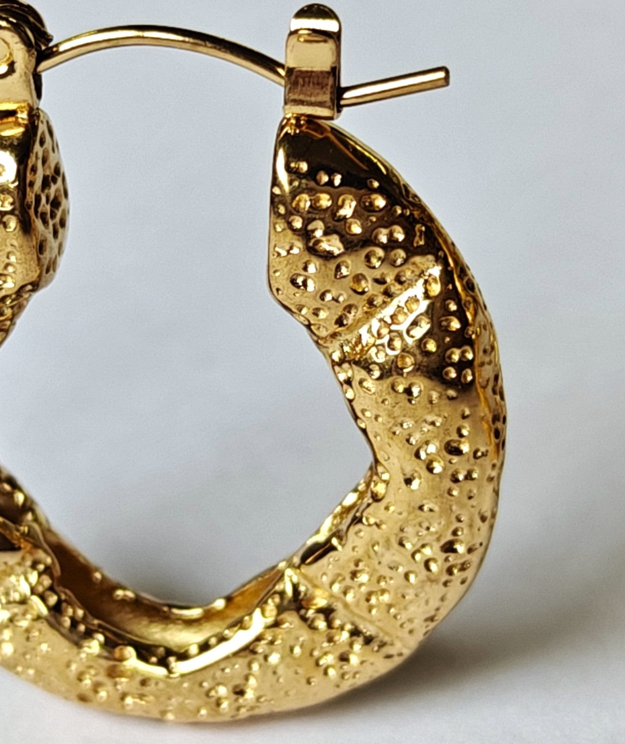 Primer plano de la textura efecto roca de los pendientes de aro Roccia en acero con baño de oro de 18k de MALBAE