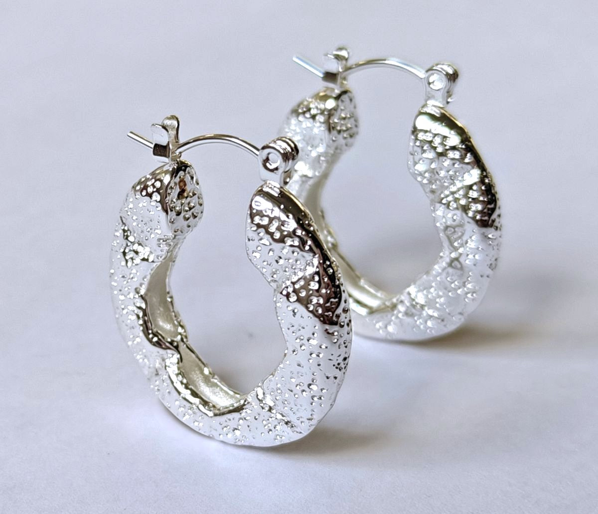 Pareja de pendientes de aro Roccia en acero inoxidable natural con acabado texturizado martilleado de MALBAE.