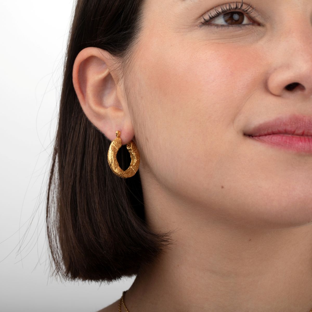 Modelo luciendo los pendientes de aro grueso Roccia de acero inoxidable waterproof bañados en oro de 18k de MALBAE.