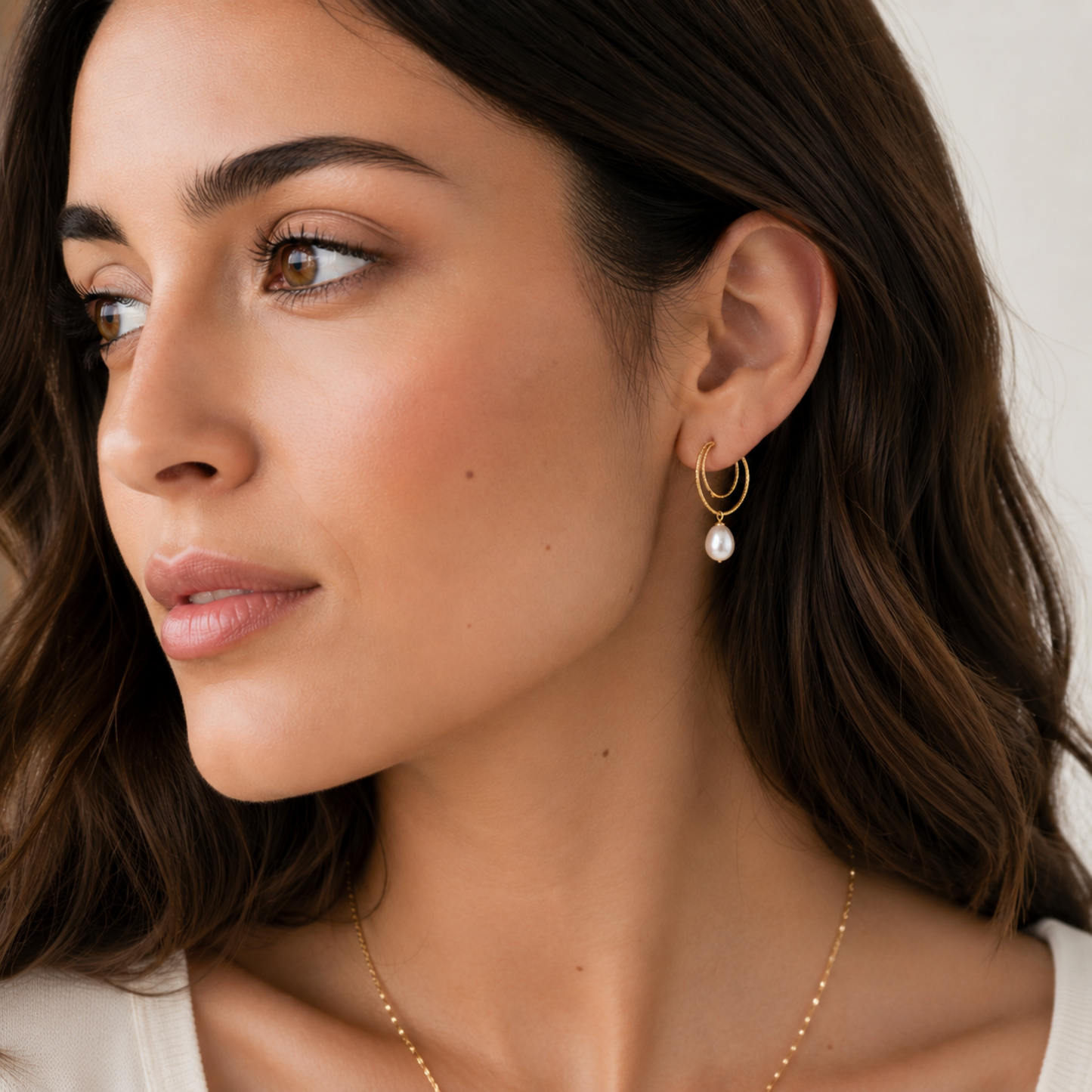 Modelo luciendo pendientes DOUX dorados con doble aro texturizado y perla cultivada